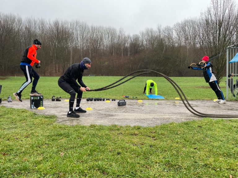 Drei Sportler trainieren mit Seilen auf einer grauen, nassen Fläche im Freien. Bootcamp, Functional Fitness, Group Fitness